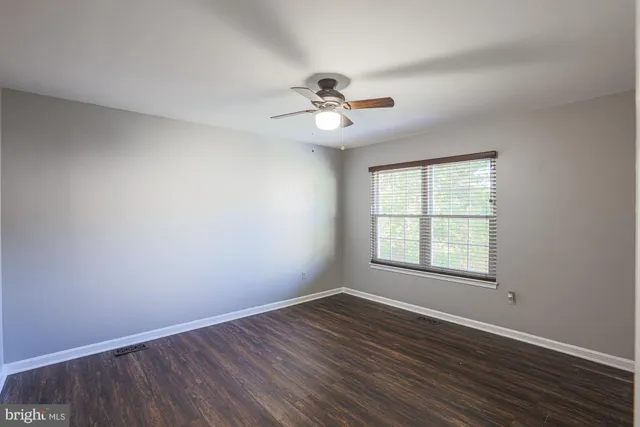 an empty room with wooden floor ceiling fan and windows