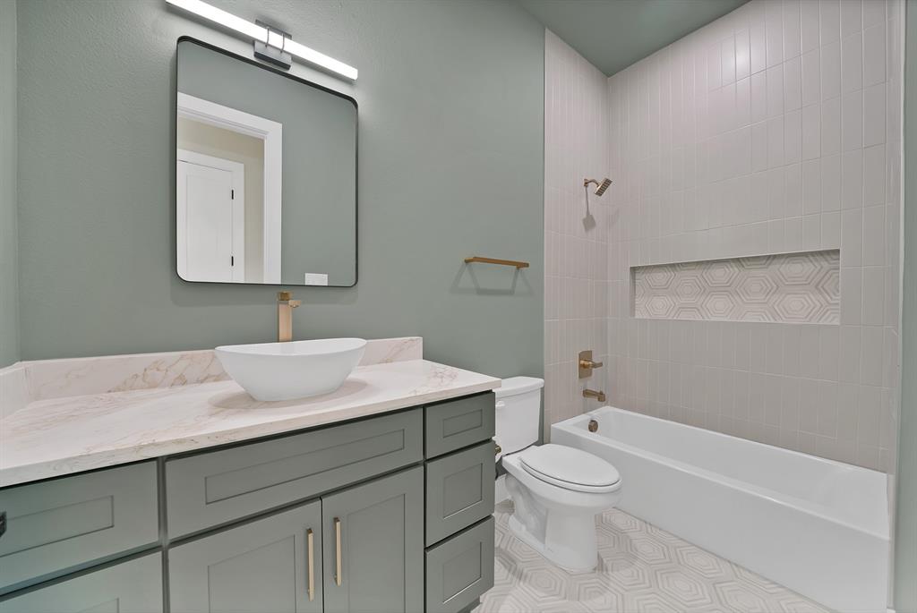 1415 Fayette Street Dallas, TX 75203 - Photo 35 of 40 Vanity with a vessel sink and gold-tone faucet, framed mirror with integrated lighting, built-in bathtub with shower, tiled shower surround with a decorative niche, and patterned floor tile