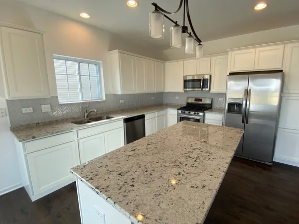 a kitchen with stainless steel appliances granite countertop a sink a stove a refrigerator a microwave oven with white cabinets