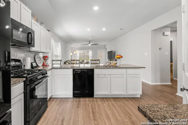 a kitchen with stainless steel appliances granite countertop a stove top oven a sink dishwasher and white cabinets with wooden floor