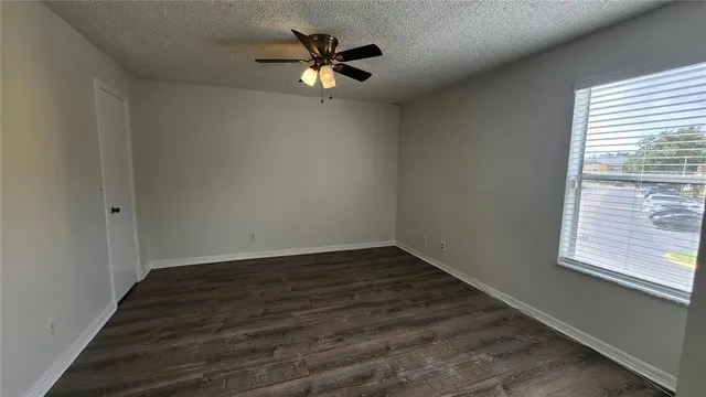 an empty room with wooden floor fan and windows