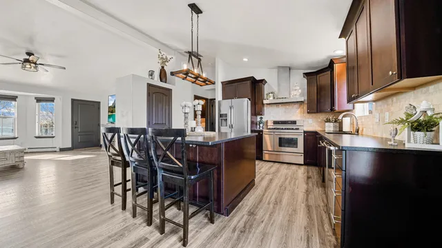 a kitchen with stainless steel appliances granite countertop a refrigerator a sink dishwasher a stove and a dining table with wooden floor