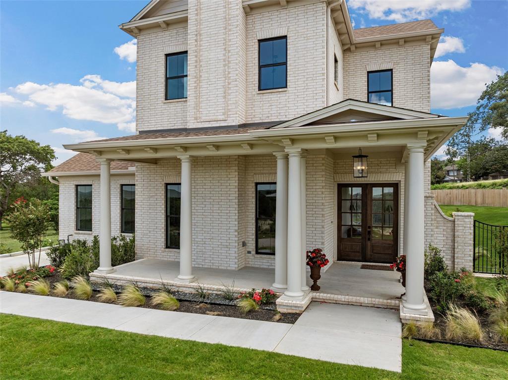 20 Ritchie Road Woodway, TX 76712 - Photo 3 of 40 White brick exterior with black-framed windows, a covered entry porch with columns, dark wood-finish double entry doors, and mature landscaping