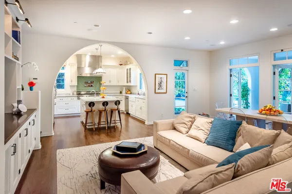 a kitchen with kitchen island granite countertop a sink a stove a refrigerator and white cabinets with wooden floor
