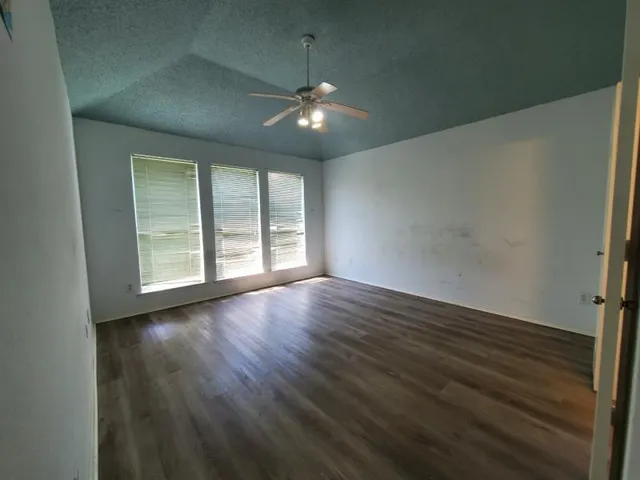a view of an empty room with wooden floor and fan
