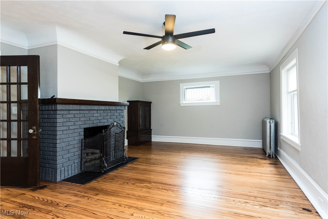 7003 Brecksville Road Independence, OH 44131 - Photo 5 of 35 Unfurnished living room featuring light wood-style flooring, radiator heating unit, crown molding, a fireplace, and ceiling fan