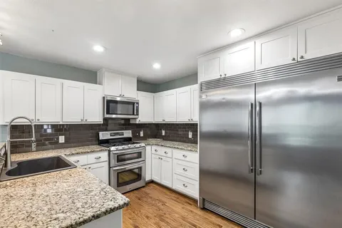 a kitchen with stainless steel appliances granite countertop a refrigerator a stove and a sink with wooden floor