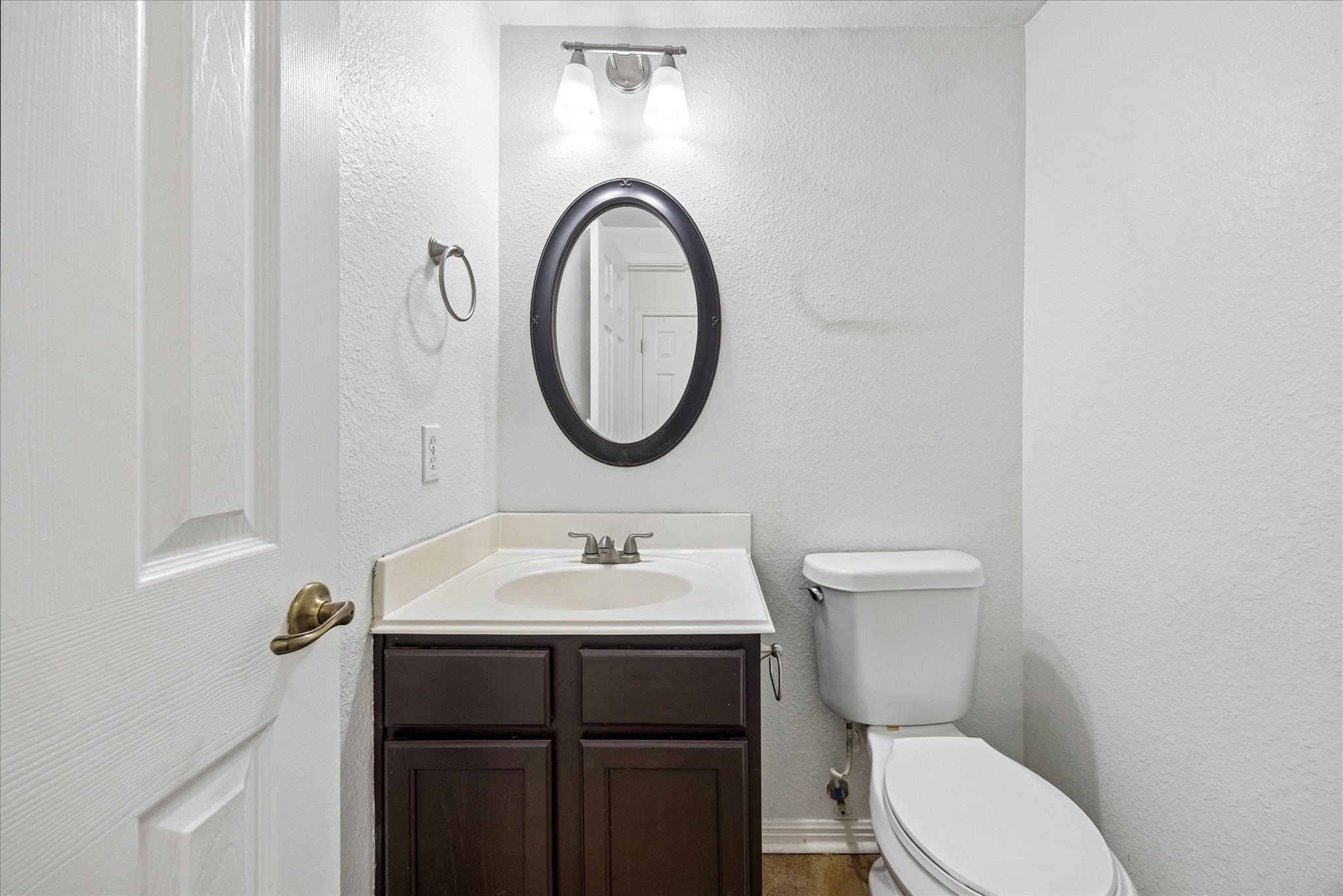 124 Lago Grande Drive Kyle, TX 78640 - Photo 13 of 16 Compact bathroom featuring a dark wood-finish vanity with an integrated sink, a matching oval framed mirror, and a two-bulb wall sconce