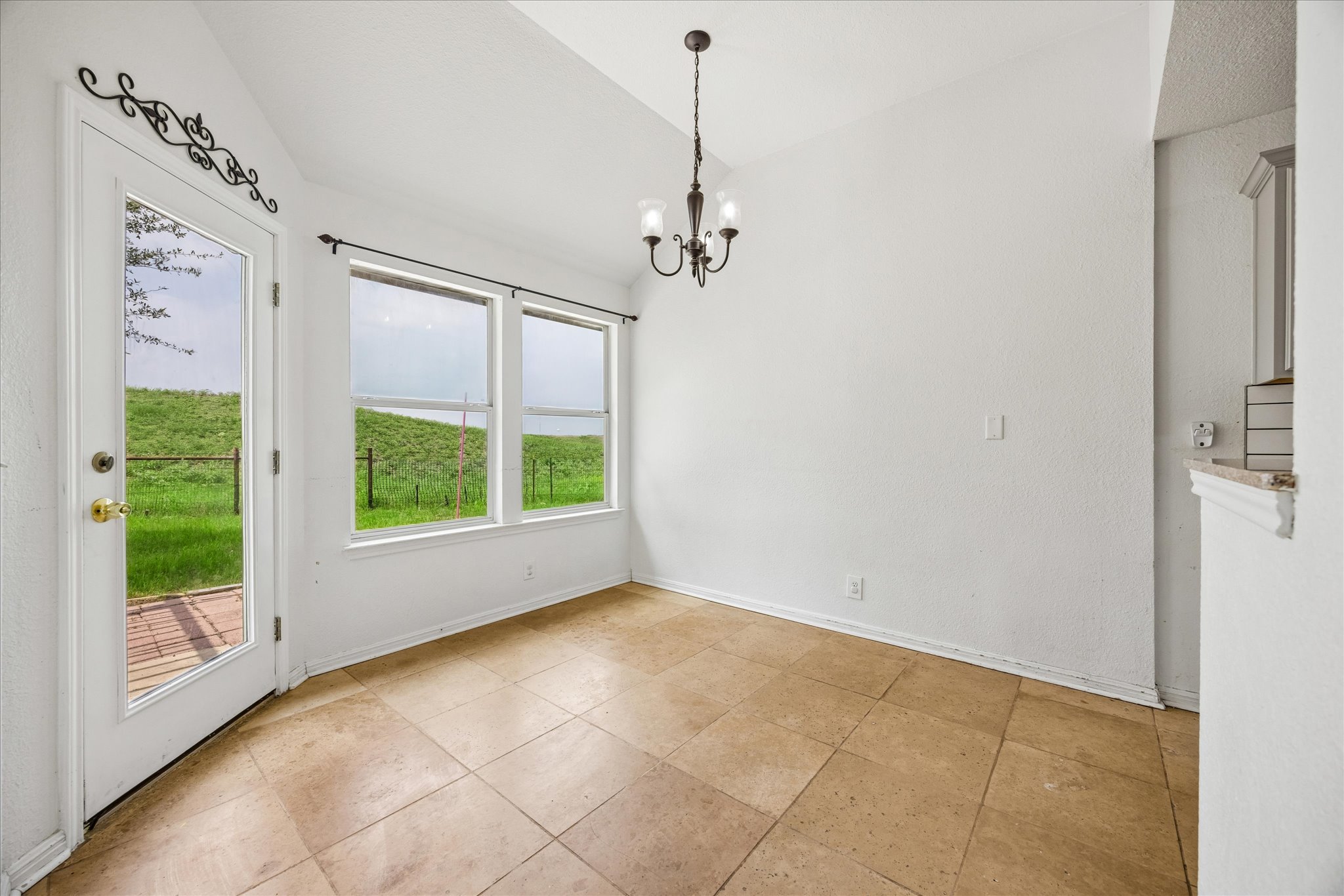 124 Lago Grande Drive Kyle, TX 78640 - Photo 4 of 16 Tiled flooring throughout a bright room featuring a decorative chandelier, multiple windows, and a glass-paneled door opening to a brick patio