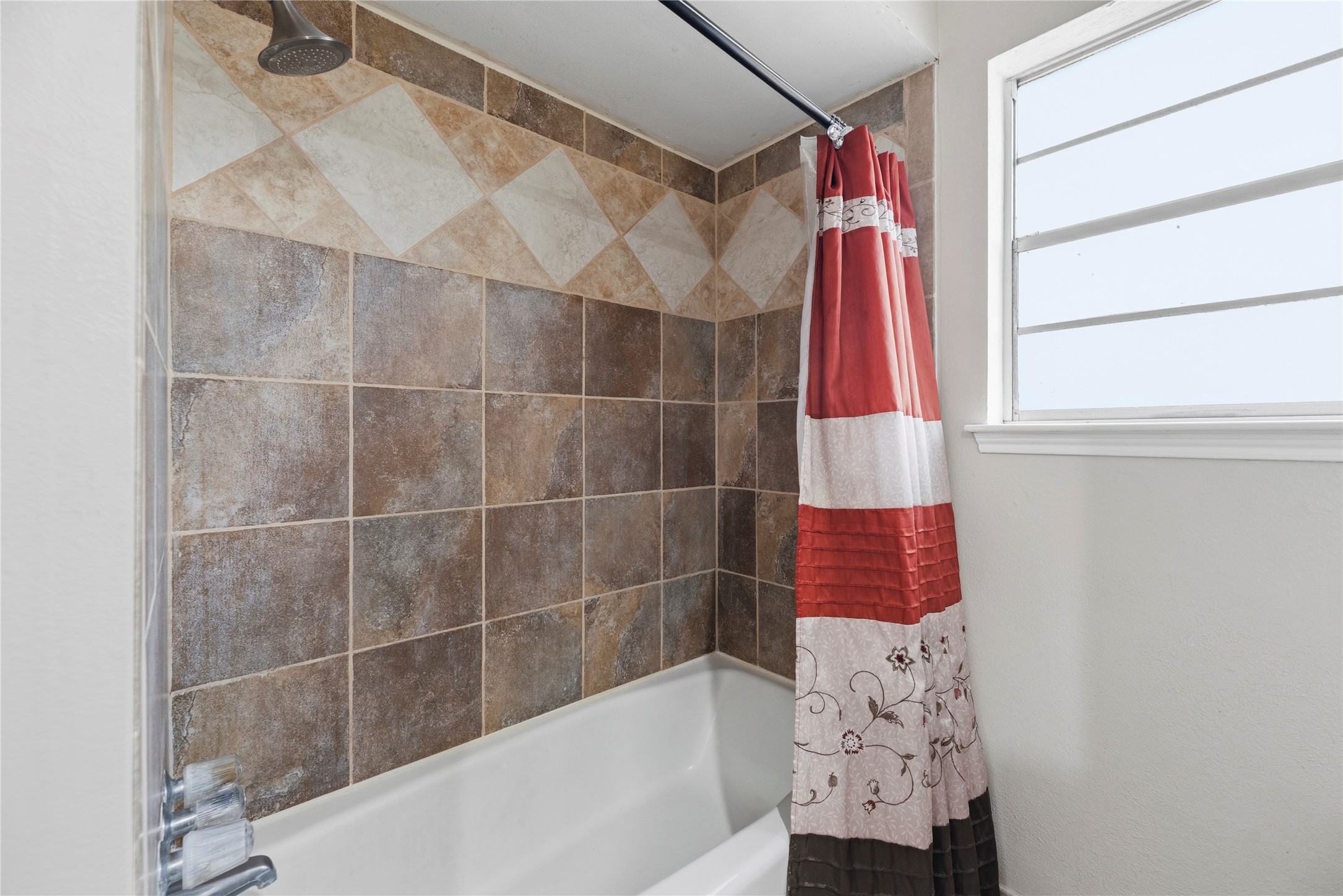 14203 Wickersham Lane Houston, TX 77077 - Photo 14 of 25 Full tub-and-shower combination featuring classic multi-toned ceramic wall tile with an elegant diagonal accent border, alongside a frosted window that delivers natural light.