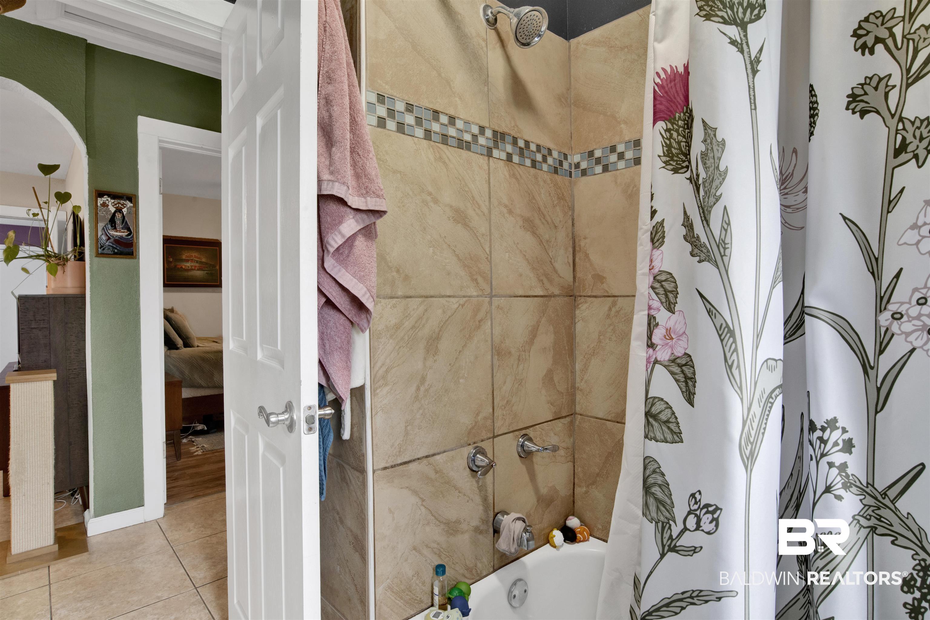 1100 North Pine Street Foley, AL 36535 - Photo 16 of 30 Tub-shower combination featuring neutral-toned wall tiles, a decorative mosaic accent strip, and a chrome showerhead