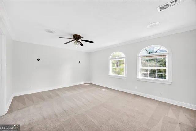 an empty room with chandelier fan and windows