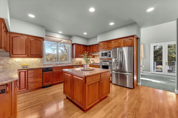 a kitchen with stainless steel appliances granite countertop a stove top oven a refrigerator a sink and dishwasher with wooden floor