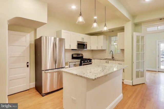 a kitchen with granite countertop a refrigerator a sink a stove a microwave and island with wooden floor