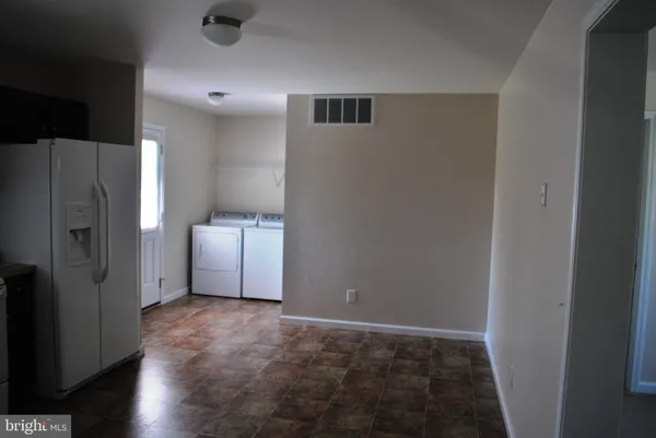 a view of a refrigerator in kitchen and an empty room with wooden floor windows