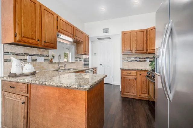 a kitchen with stainless steel appliances granite countertop a refrigerator a sink dishwasher and wooden cabinets with wooden floor