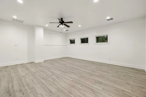 a view of an empty room with wooden floor and a ceiling fan