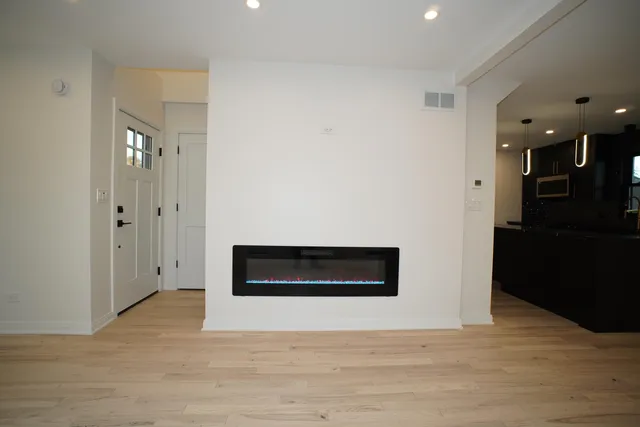 a view of an empty room with wooden floor and a kitchen