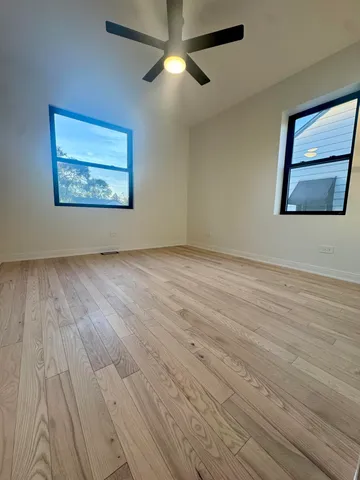 an empty room with wooden floor chandelier fan and windows