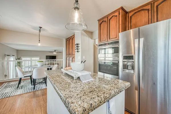 a kitchen with stainless steel appliances granite countertop a refrigerator a sink dishwasher a dining table and chairs with wooden floor