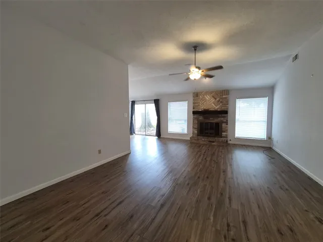 an empty room with wooden floor a chandelier fan and windows