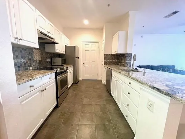 a large kitchen with granite countertop a stove top oven a sink a granite counter space and cabinets