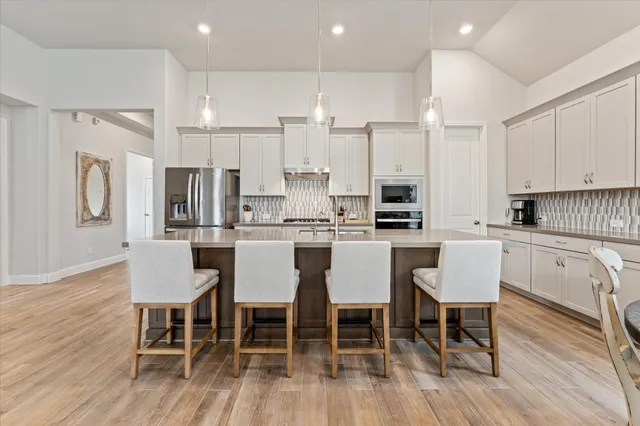a kitchen with stainless steel appliances granite countertop a dining table chairs refrigerator and cabinets