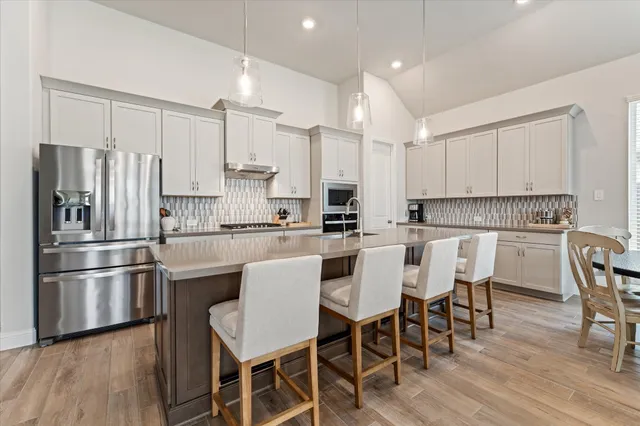 a kitchen with stainless steel appliances a refrigerator a stove a dining table and chairs with wooden floor