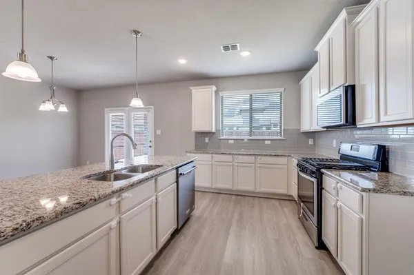 a kitchen with stainless steel appliances granite countertop wooden cabinets a sink dishwasher a stove and a refrigerator with wooden floor