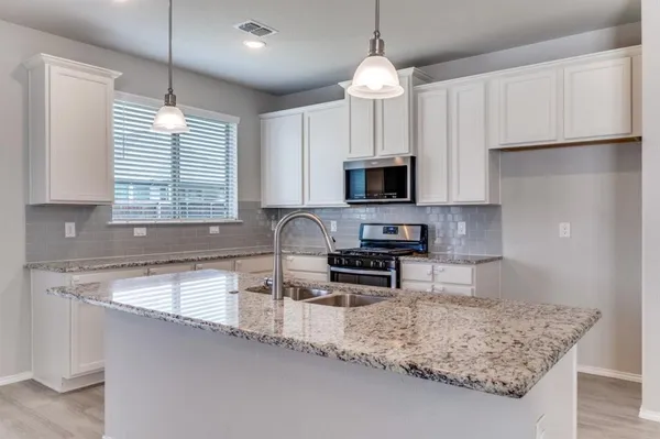 a kitchen with stainless steel appliances granite countertop a sink a stove a microwave a refrigerator a center island and cabinets