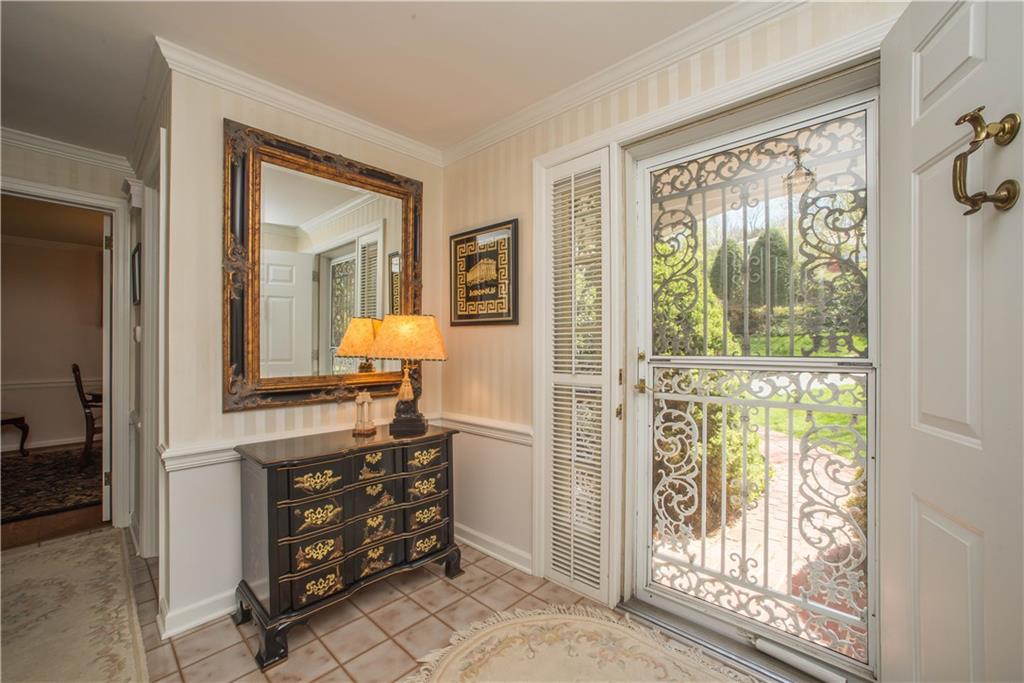 The front entry has an elegant wrought iron storm door, sidelights with louvered blinds, and an all-wooden front door. The tiled foyer offers chair rail trim and crown moldings.