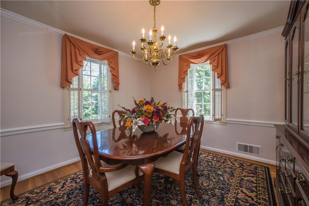 The same oak flooring is also found in the formal dining room, outfitted with chandelier, crown molding, and chair rail trim. Windows on two walls allow natural light to fill the space, creating an inviting atmosphere.