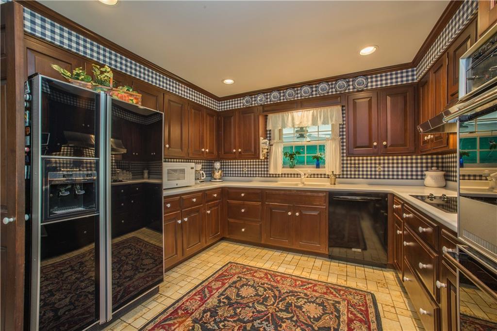 The custom-designed kitchen features solid cherry Rutt cabinetry and a molded Corian countertop, offering a seamless and sleek work surface. Flooring is ceramic tile and the appliances are black glass. The window above the double sink looks onto the upper, covered patio.