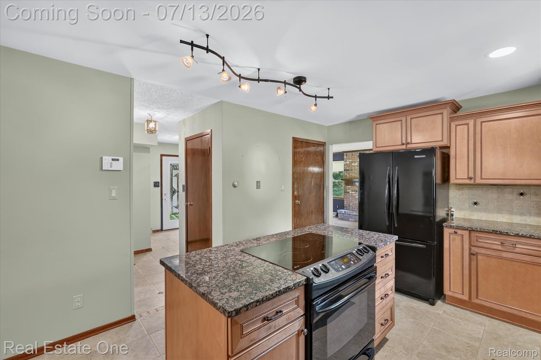 6039 Fish Lake Road Holly, MI 48442 - Photo 13 of 70 Kitchen featuring a central island with an integrated cooktop, granite countertops, wood-finish cabinetry, black appliances, and updated lighting.