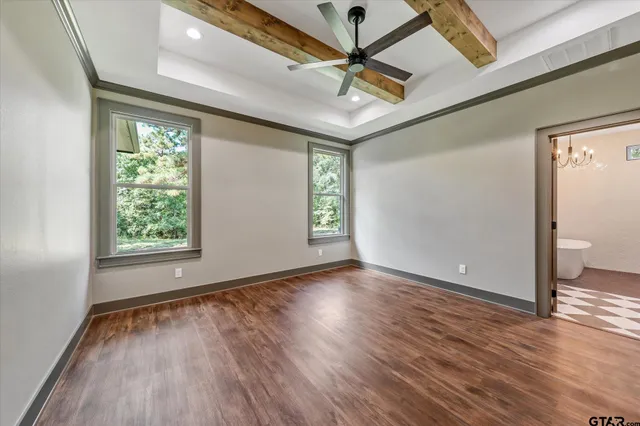 an empty room with wooden floor chandelier fan and windows