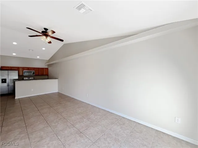 an empty room with kitchen view and a ceiling fan