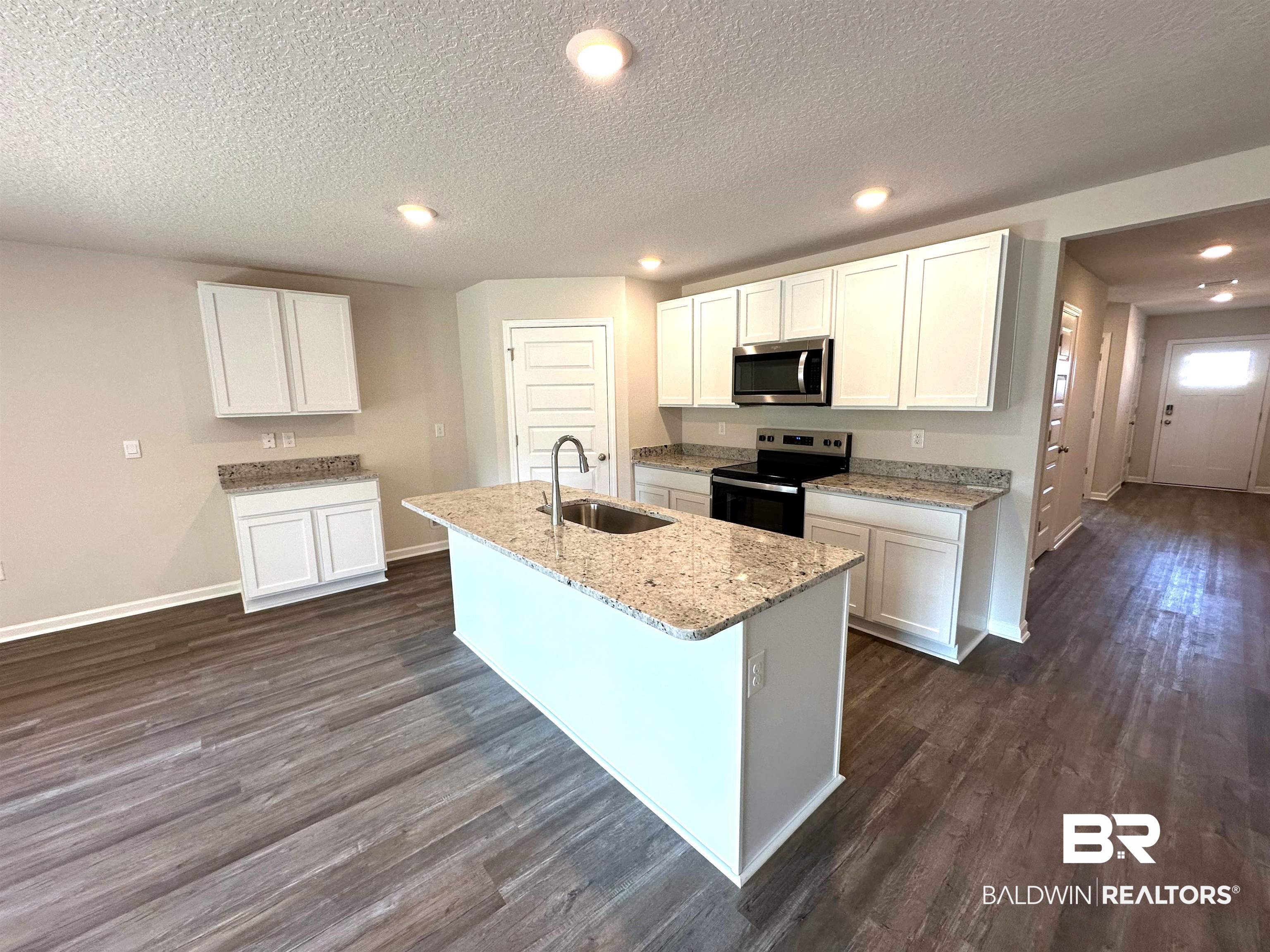Kitchen featuring dark wood-type flooring, white cabinetry, an island with sink, and stainless steel appliances