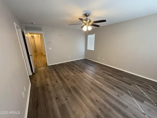 an empty room with wooden floor fan and windows