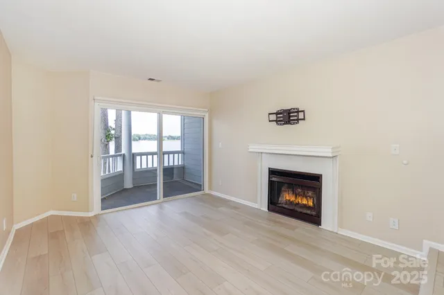 a view of an empty room with wooden floor fireplace and a window