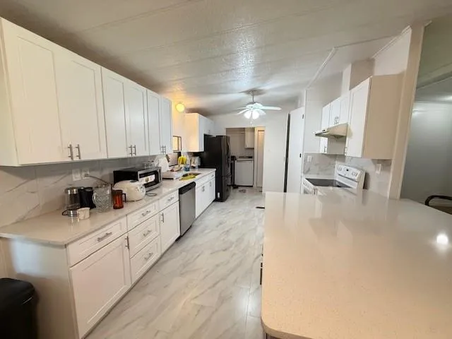 a large white kitchen with cabinets a sink a window and stainless steel appliances