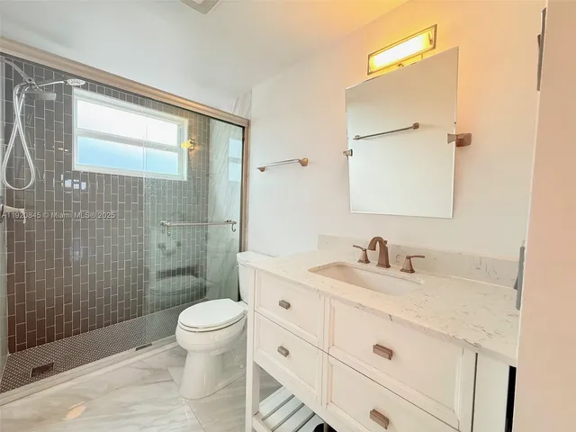 a bathroom with a granite countertop toilet a sink a mirror a window and a shower