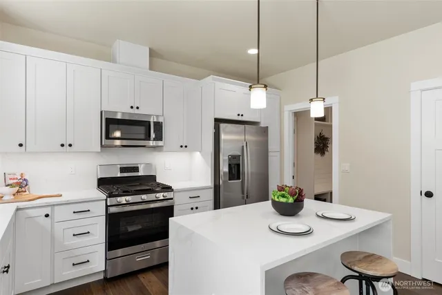 a kitchen with stainless steel appliances kitchen island granite countertop a sink a stove a refrigerator and white cabinets with wooden floor