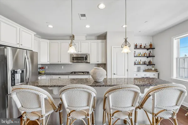 a kitchen with granite countertop a dining table chairs refrigerator and microwave
