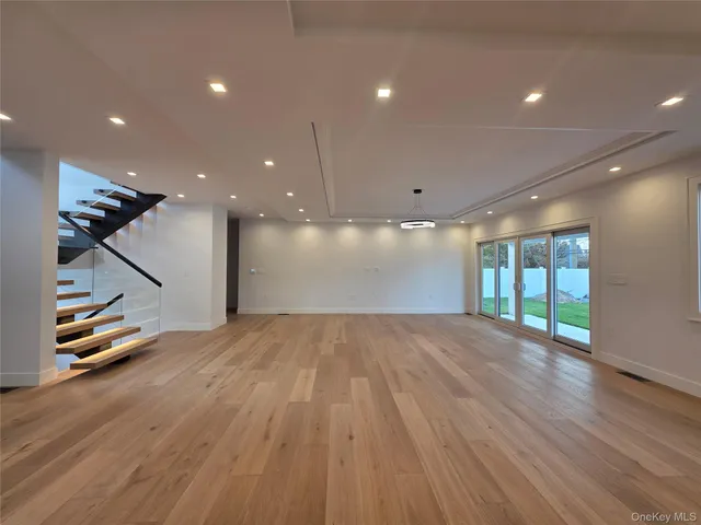 a view of an empty room with wooden floor a kitchen and windows