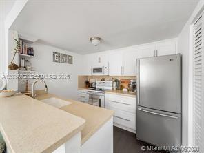 4590 Southwest 68th Ct Circle, Unit 8 Miami, FL 33155 - Photo 3 of 11 a kitchen with a refrigerator a stove a sink and white cabinets
