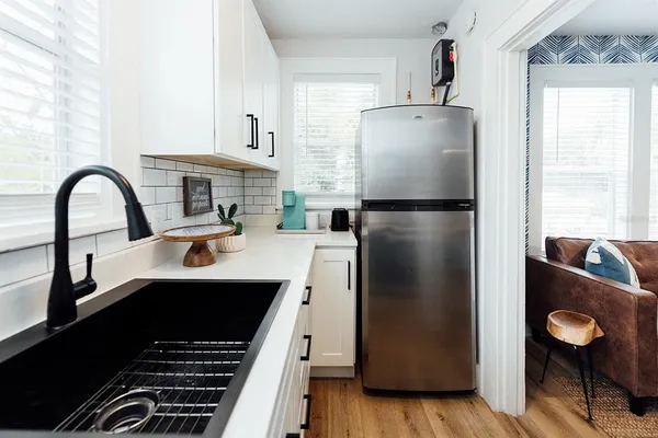 a kitchen with stainless steel appliances granite countertop a refrigerator a sink and white cabinets with wooden floor