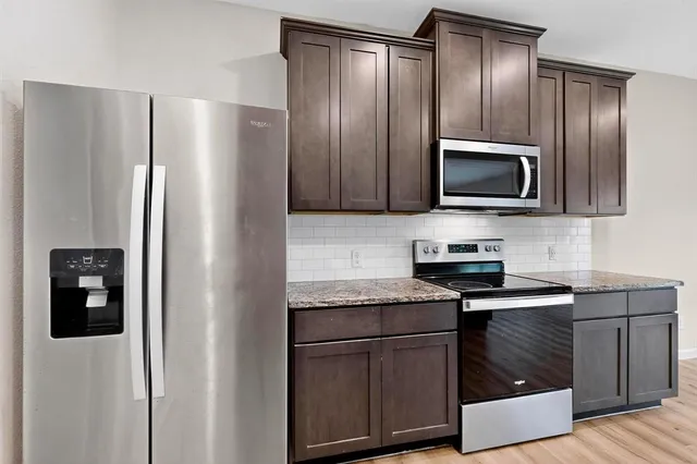 a kitchen with stainless steel appliances granite countertop wooden cabinets a sink and dishwasher with wooden floor