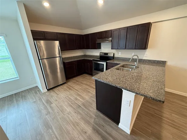a kitchen with granite countertop a refrigerator a sink and wooden cabinets