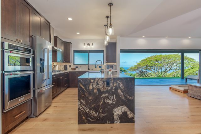 a kitchen with stainless steel appliances kitchen island granite countertop a refrigerator oven a sink with wooden cabinets and wooden floor