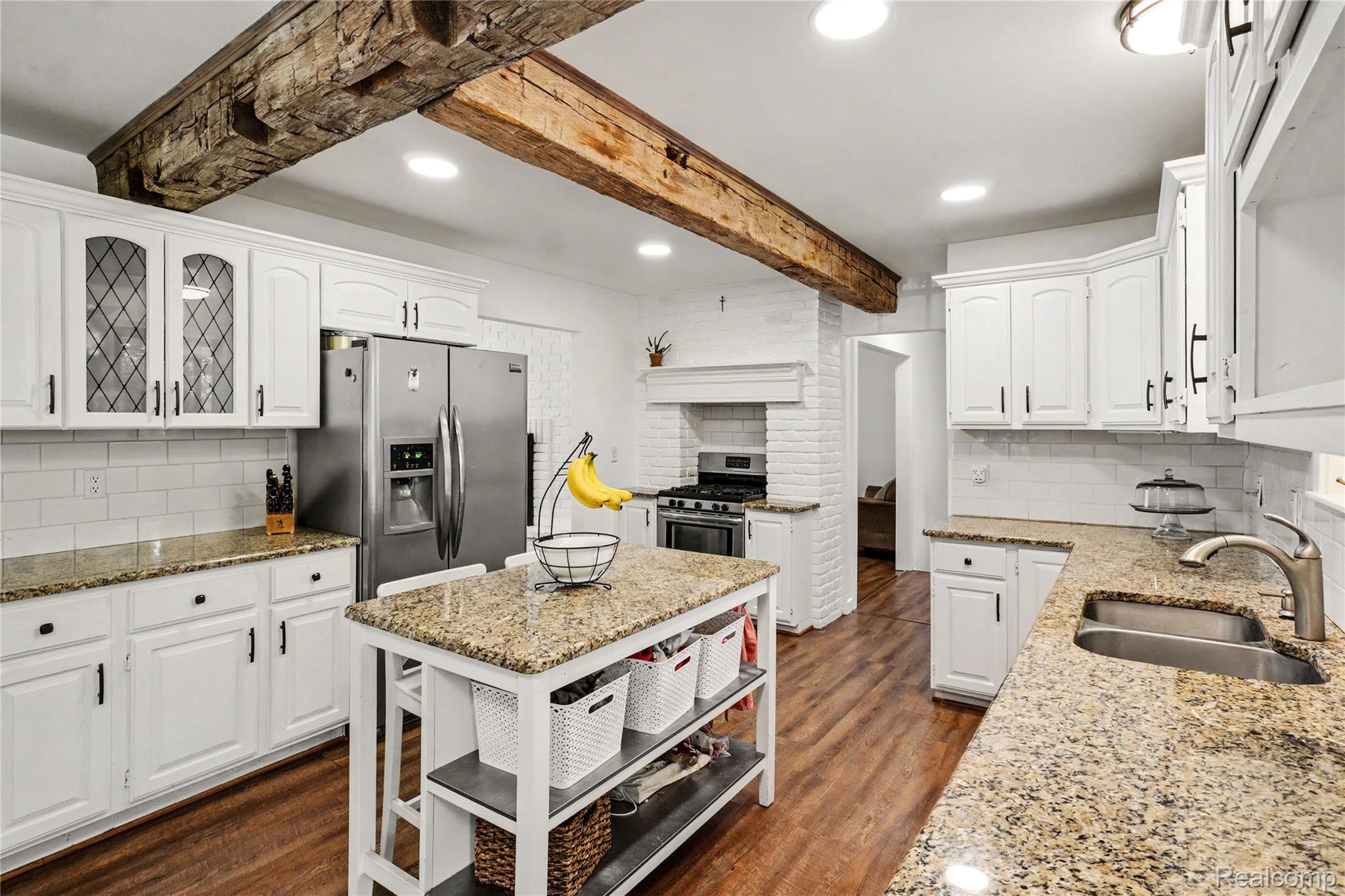 5465 South Lake George Road Metamora, MI 48455 - Photo 13 of 61 Kitchen featuring hardwood flooring, exposed ceiling beams, white cabinetry with black hardware, granite countertops, and stainless steel appliances